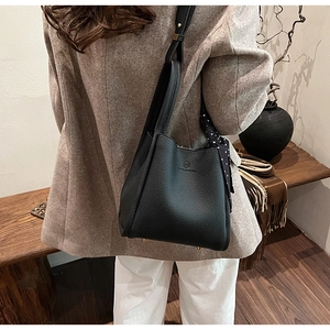 Detail of black lychee grain leather bucket bag with polka dot scarf on a model