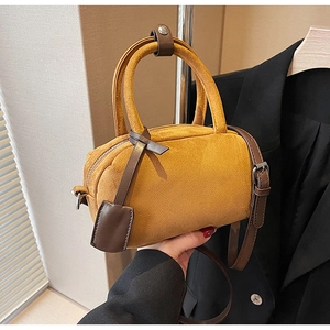 Detailed close-up of a mustard suede cylinder bag with dark brown leather handles
