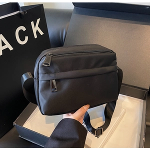 Detail view of black nylon crossbody bag with multiple zippers and wide strap in gift box