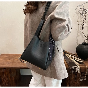 Detail of black pebbled leather bucket bag featuring a decorative polka dot silk scarf