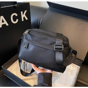 Detail of minimalist black nylon crossbody bag with zipper pockets and gift box packaging