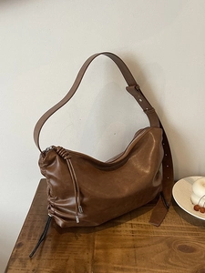 Deep brown leather shoulder bag with minimalist knot detail on a wooden table