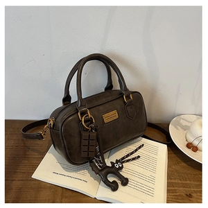 Dettaglio borsa Boston vintage marrone scuro con ciondoli a gatto su un libro