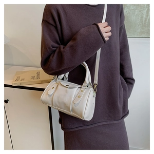 Detail of off-white cylindrical crossbody bag with fine PU texture and metal rivet accents