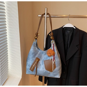 Detail of blue denim tote bag with brown leather straps and plush puppy charm