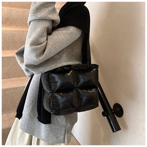 Close-up of a black quilted puffer tote bag in glossy nylon on a female model's shoulder