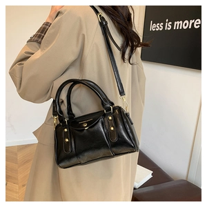 Detail view of a black glossy handbag with gold rivets and chain strap on a trench coat