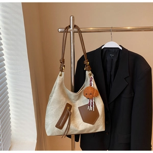 Detail view of large cream tote bag with brown straps and cute teddy bear keychain
