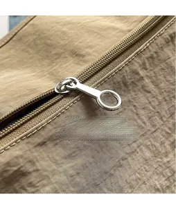 Detail of smooth metal zipper pull on khaki nylon bag with wrinkled fabric texture