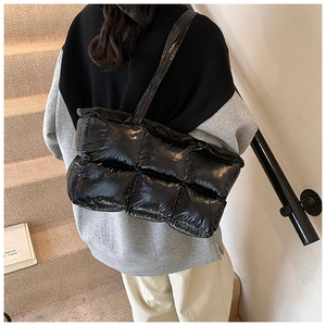 Back view of a model wearing a black glossy quilted puffer tote bag on the shoulder