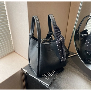 Detail of black lychee leather bucket bag featuring polka dot scarf on handle and embossed logo