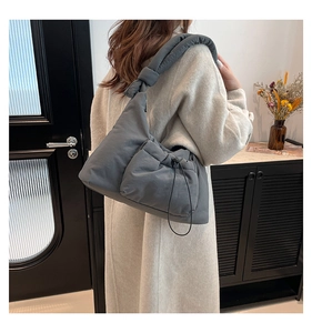 Close-up of dark grey quilted nylon crossbody bag with drawstring pocket and knotted strap