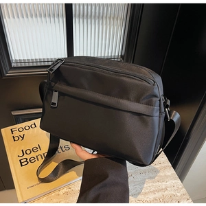 Close-up of minimalist black crossbody bag showing multi-zip pockets and nylon texture