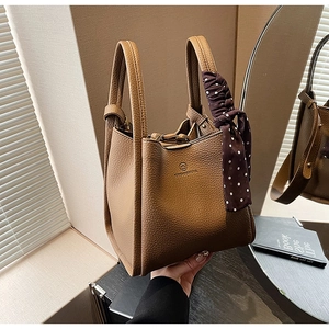 Detail of brown litchi pattern leather bucket bag with decorative polka dot silk scarf
