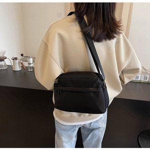 Detail of a black nylon crossbody bag with multiple zippers and adjustable wide strap