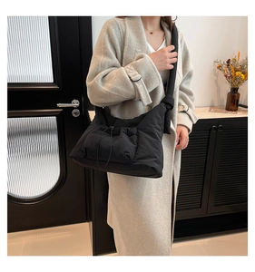 Detail of a black quilted crossbody bag featuring a drawstring pocket and knotted strap