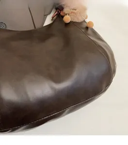 Dettaglio della borsa hobo marrone scuro con logo dorato e ciondolo in peluche