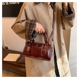 Close-up of wine red pillow bag with gold rivets worn with a beige trench coat