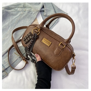 Close-up of brown leather pillow bag with gold metal plate and cute charms on denim