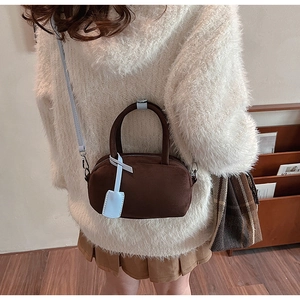 Detailed view of brown suede satchel with blue leather strap on model in cozy indoor setting