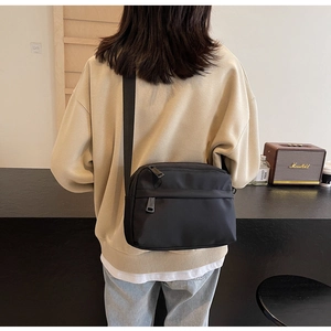 Detail of a minimalist black nylon crossbody bag with adjustable strap worn by a model