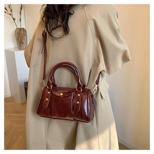 Macro detail of wine red glossy leather handbag with golden hardware on a beige coat