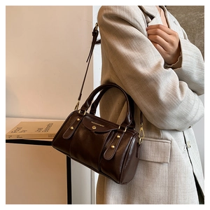 Detail of dark brown leather Boston bag with vintage gold hardware on a model's shoulder