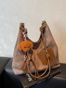 Vintage brown canvas tote bag with teddy bear charm on a black leather sofa