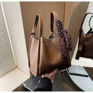 Close-up of brown lychee leather bucket bag with decorative polka dot silk scarf handle