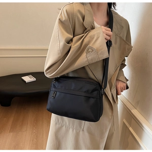 Close-up of a black nylon crossbody bag with adjustable strap on a beige trench coat