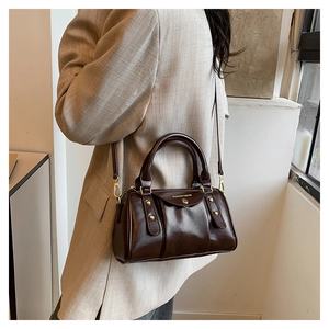 Detail view of dark brown glossy leather Boston bag with gold rivets and fashion logo