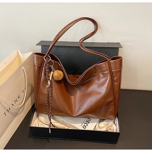 Brown leather tote bag detail with woven charm and premium black gift box packaging