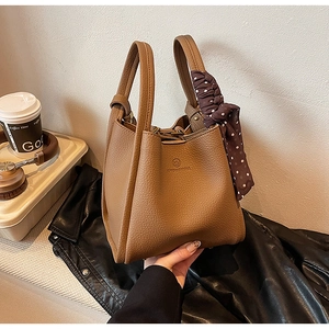 Close-up of brown lychee grain leather bucket bag with decorative silk scarf on handle