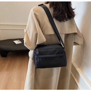 Detail of black multi-zipper crossbody bag showing nylon texture and adjustable shoulder strap