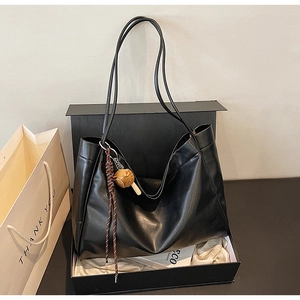 Detail of a large black soft leather tote bag with elegant charm in a gift box setup