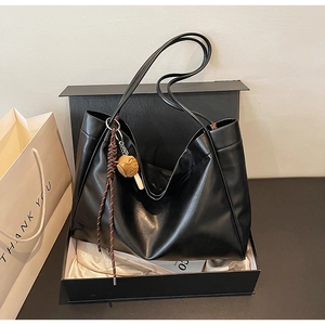 Detailed view of black faux leather tote bag in a gift box with a cartoon pendant