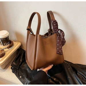 Detailed view of brown lychee grain leather bucket bag with elegant polka dot silk scarf