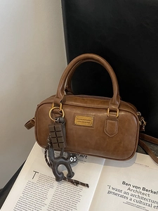 Borsa Boston vintage marrone con doppi manici e ciondoli su uno sfondo di rivista d'arte
