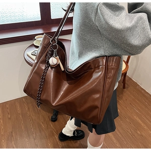 Detail of dark brown faux leather tote bag with woven strap and baseball charm on a model