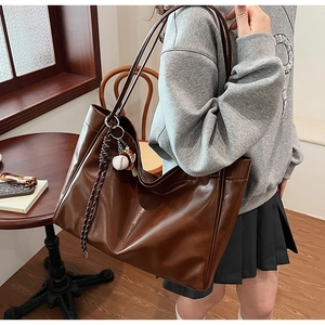 Close-up of brown PU leather tote bag featuring a white baseball charm and woven detail