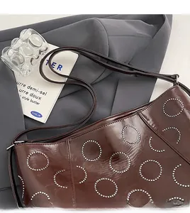 Detail of dark brown glossy leather bag featuring circular stud patterns and adjustable strap
