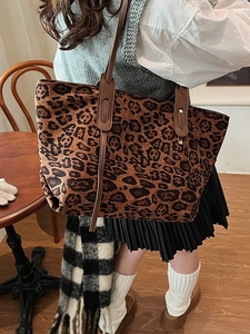 Large leopard print tote bag with brown leather straps shown in a stylish cafe setting