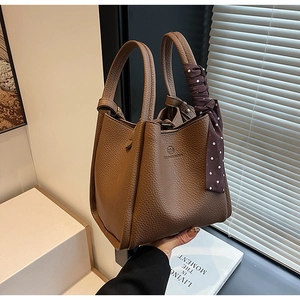Close-up of brown litchi leather bucket bag featuring decorative polka dot handle scarf