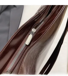 Close-up of a smooth silver metal zipper on a dark brown glossy leather tote bag