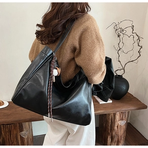 Close-up of black PU leather tote bag with woven charm on a scenic outdoor bench