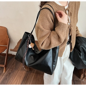 Detail view of large black tote bag with slender straps and ball charm on model