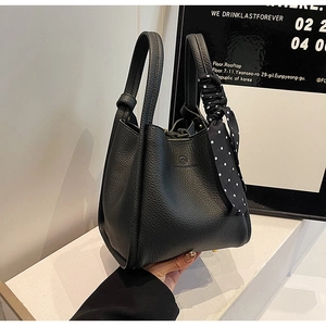 Detail of black lychee grain leather bucket bag with top handles and polka dot silk scarf