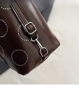 Detail of dark brown leather handbag featuring silver rivet circles and polished metal hardware