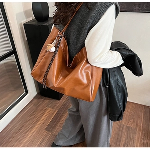 Side view of a large brown leather tote bag featuring a baseball charm and woven strap details