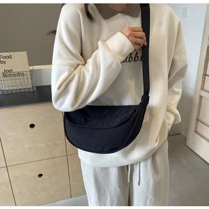 Close-up of black crossbody dumpling bag with mountain line embroidery on beige sweatshirt